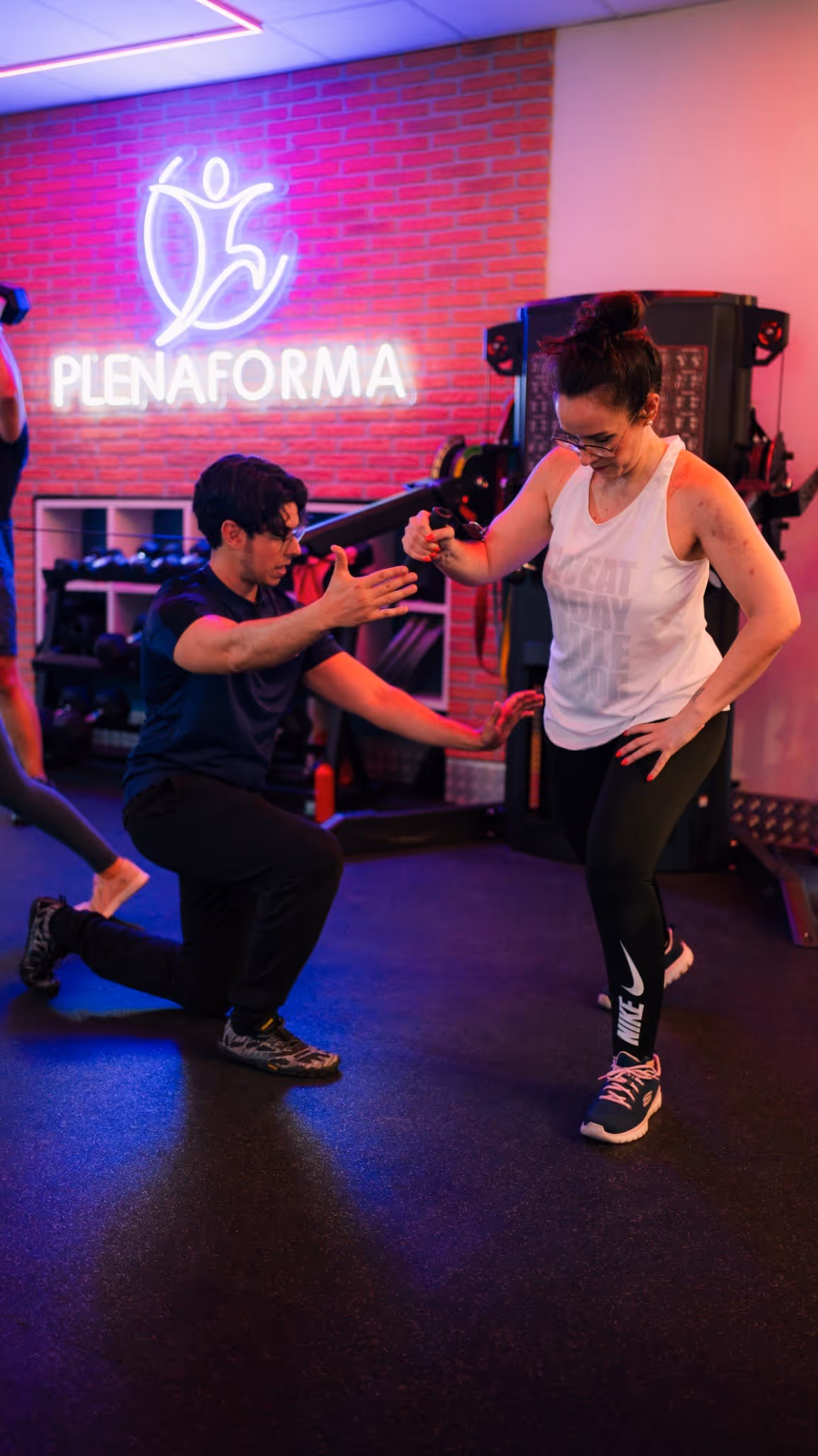 Entrenador de PlenaForma corrigiendo la postura de una clienta durante un ejercicio